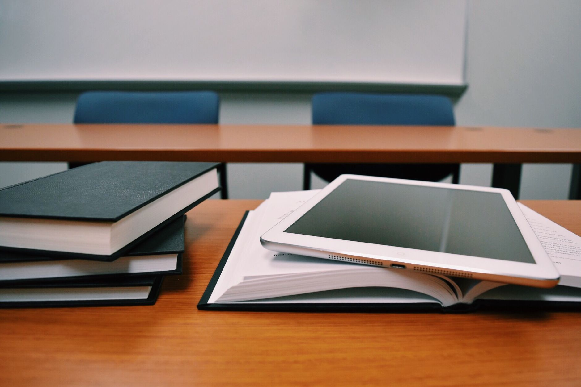 A tablet and books on a desk in a classroom.