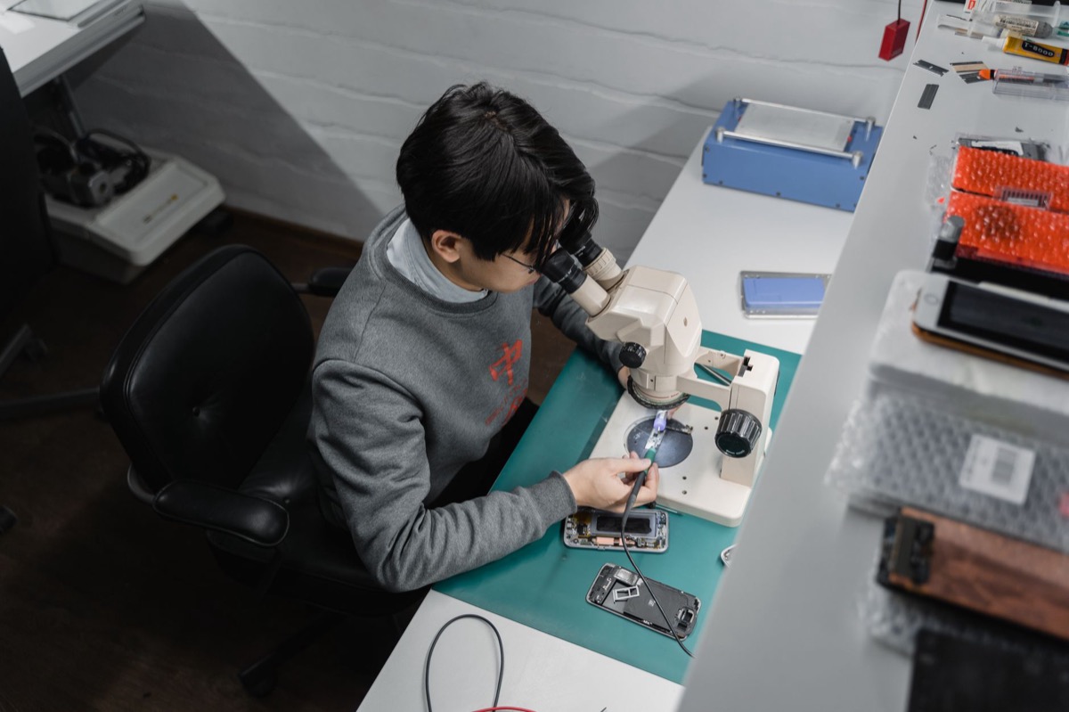 Un técnico inspecciona un teléfono inteligente bajo un microscopio en un banco de reparación.