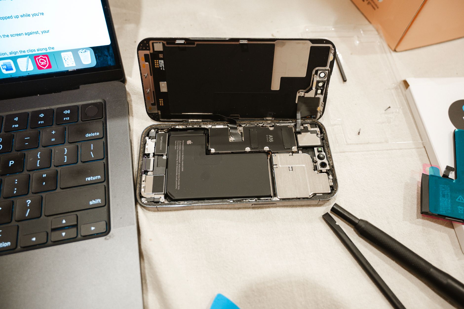 An iPhone settings screen showing battery maximum capacity next to a tray of phones being tested for wholesale.