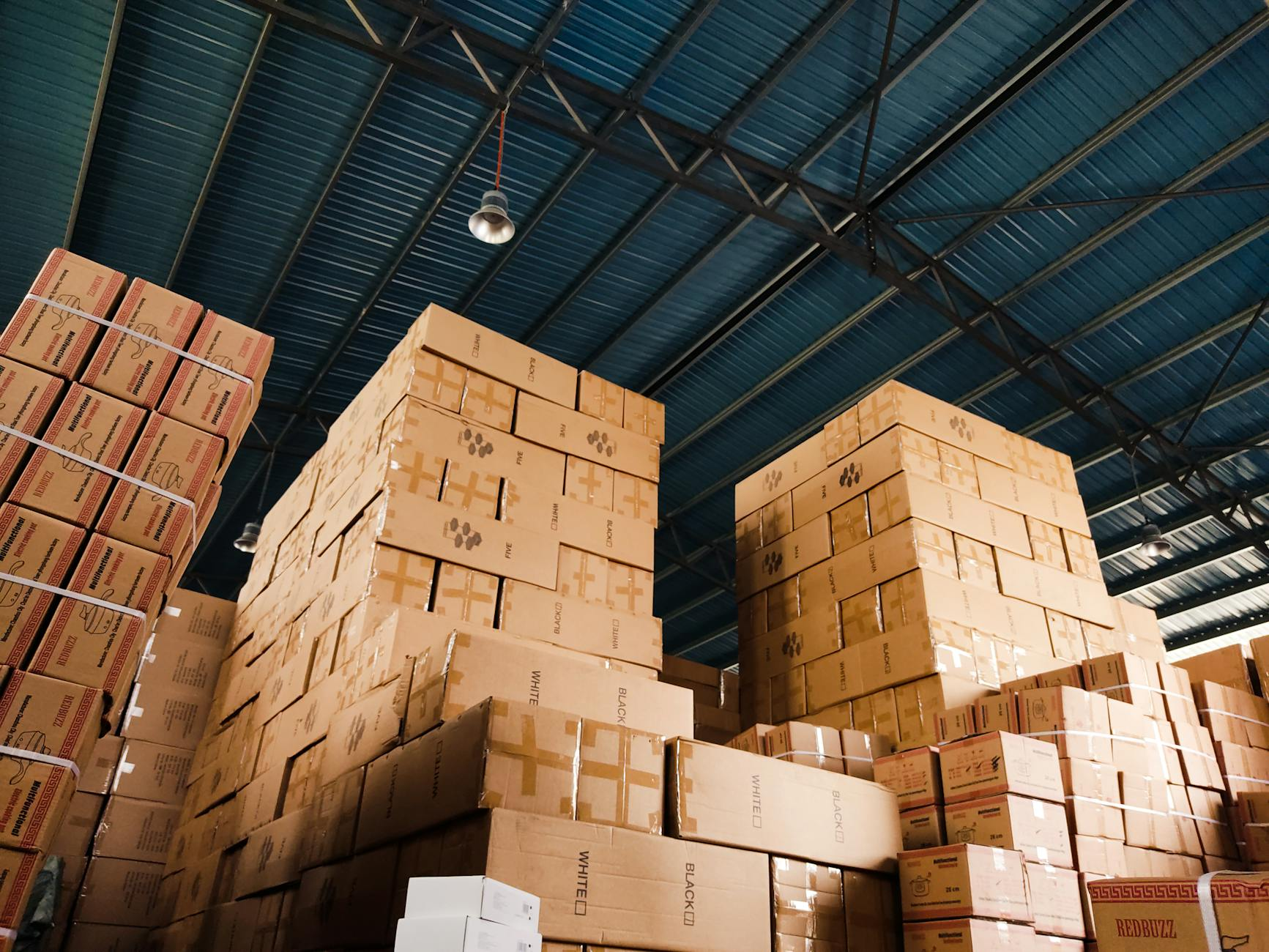 Pallets of stacked cardboard boxes in a warehouse aisle, illustrating minimum order quantity inventory in wholesale electronics.