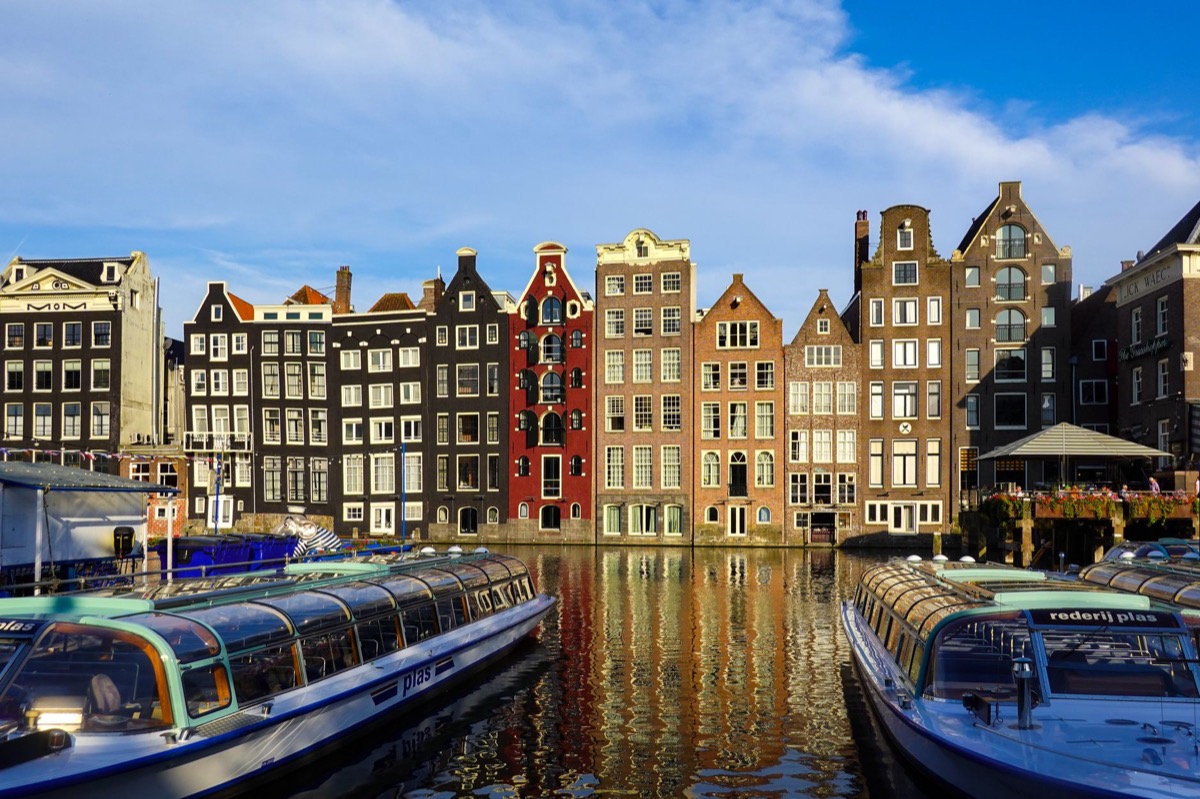 Coloridos edificios históricos a lo largo de un canal de Ámsterdam con barcos en primer plano.