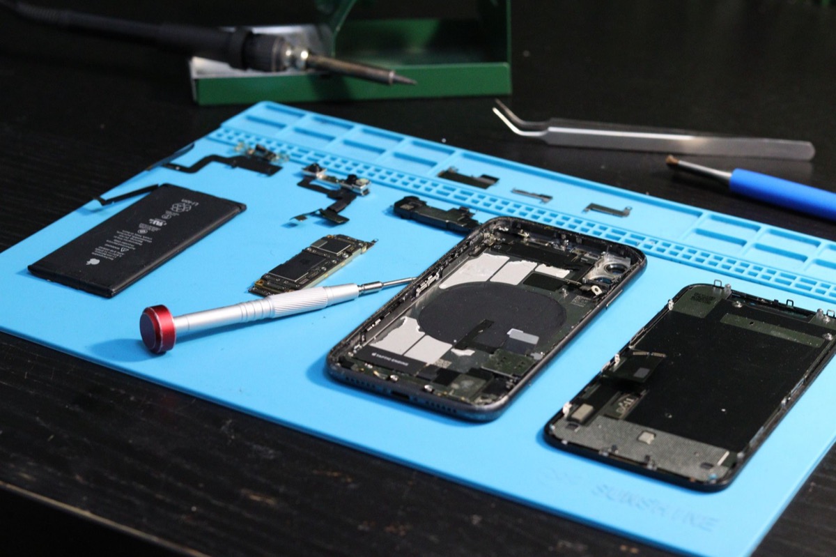 Primer plano de piezas de teléfonos inteligentes desmontadas sobre una alfombra de reparación con herramientas.