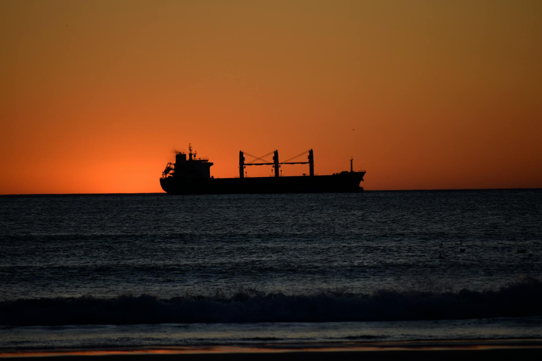 Cargo ship sailing on the open ocean at sunset, illustrating the shipping routes through the Strait of Hormuz that affect wholesale electron