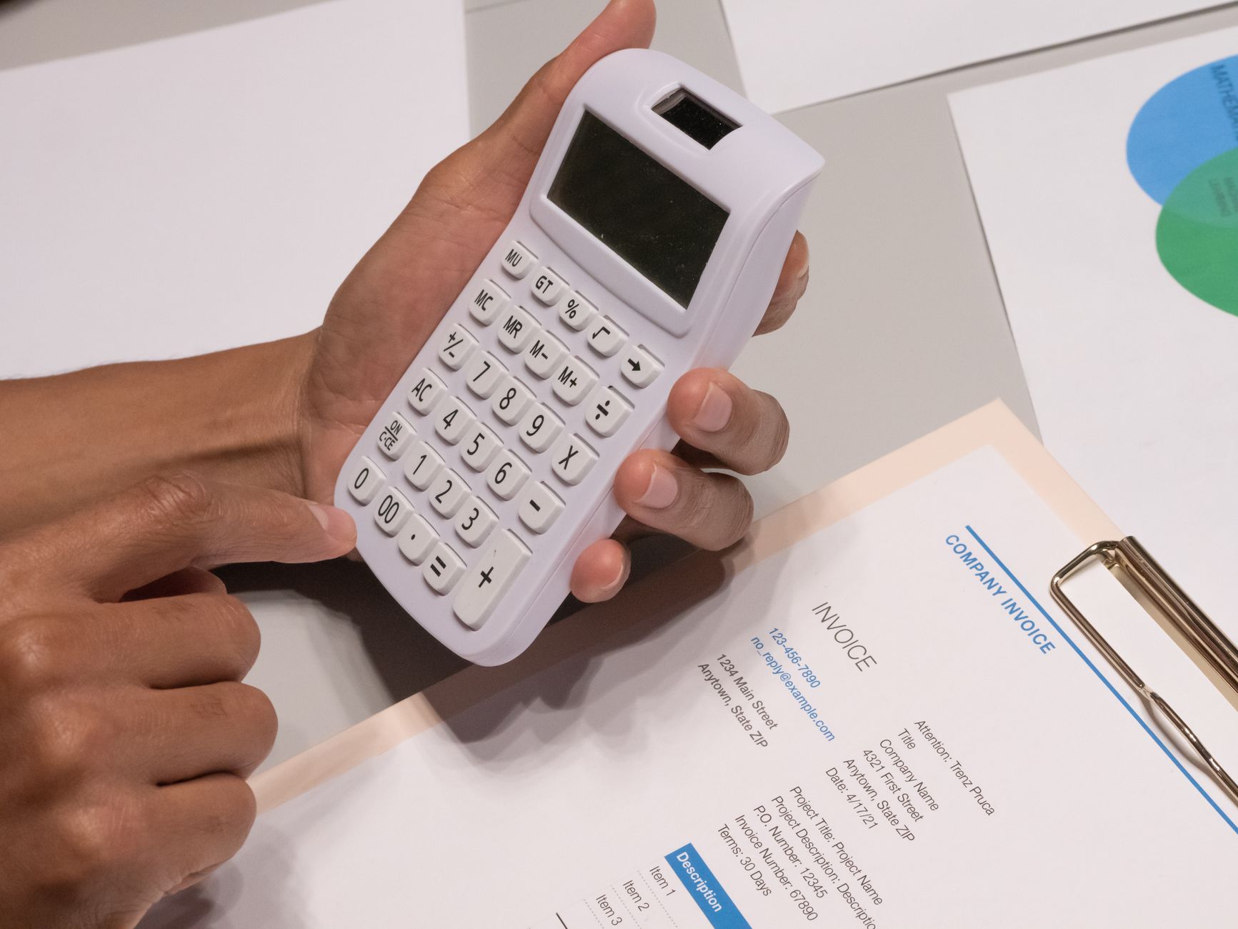 Hands using a calculator next to an invoice on a desk.