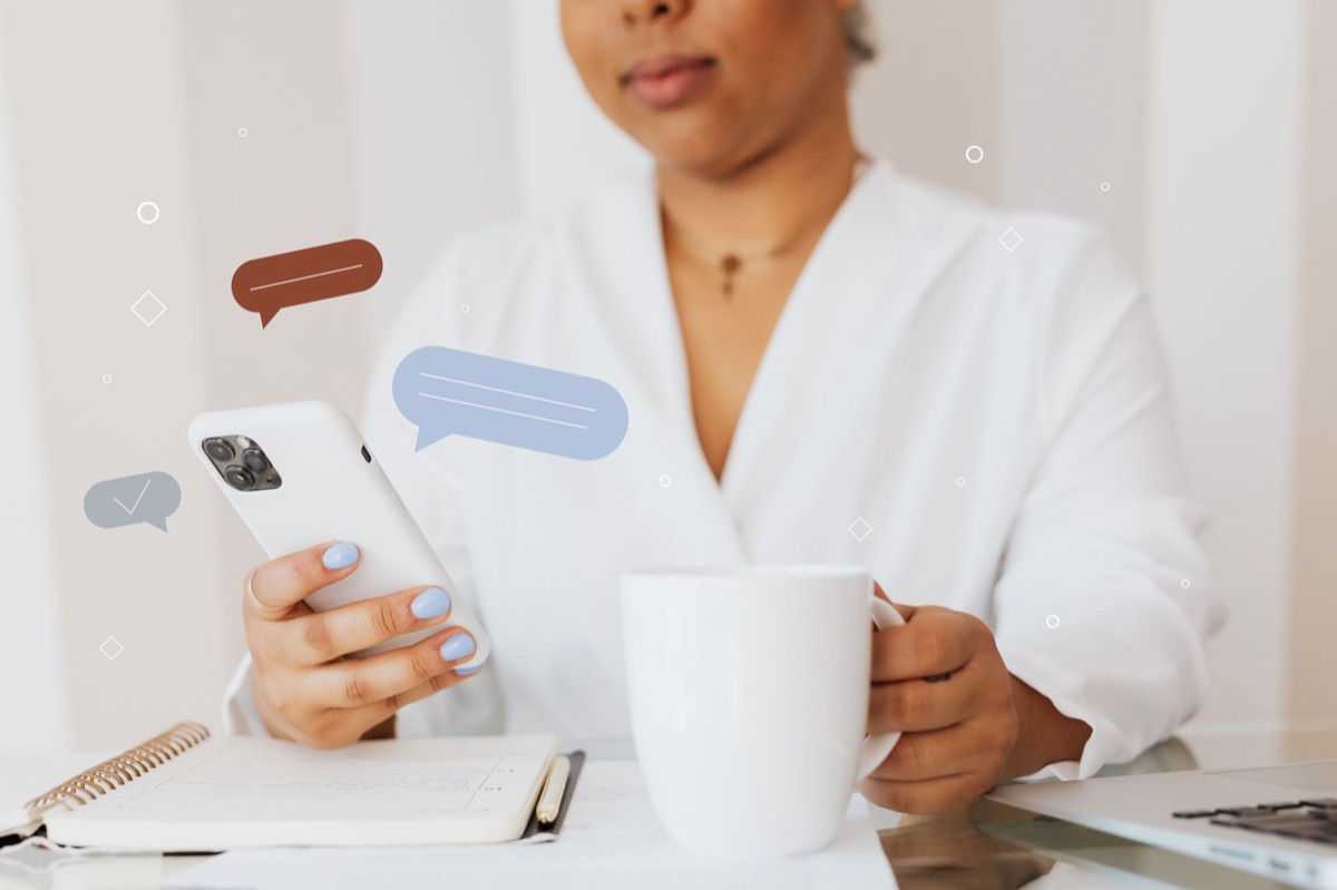 Primer plano de una persona que usa un teléfono inteligente mientras sostiene una taza de café.