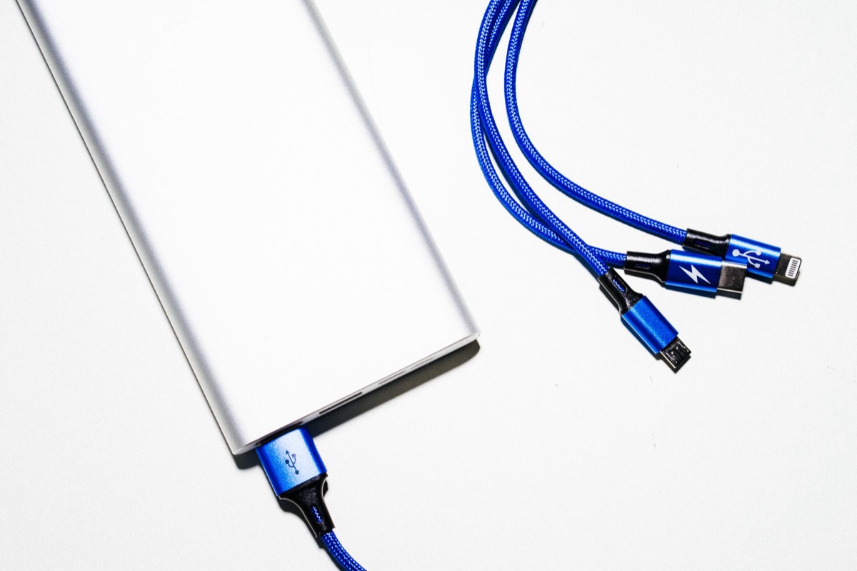 Una toma minimalista de un banco de energía con cables de carga USB azules sobre un fondo blanco.